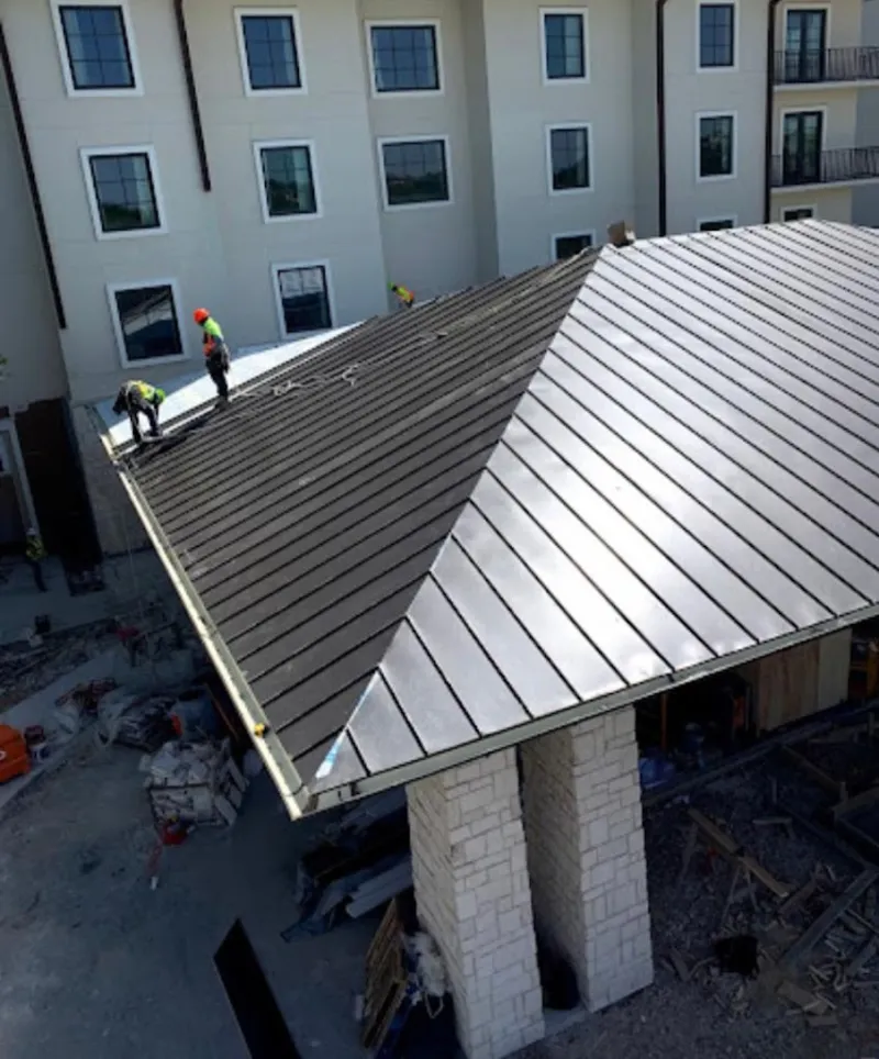 Crew installing standing seam metal roof panels on a commercial project in West Bloomfield